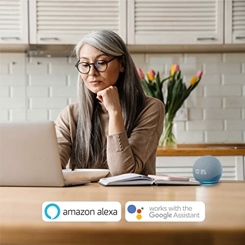 Woman using laptop with smart assistant device on table